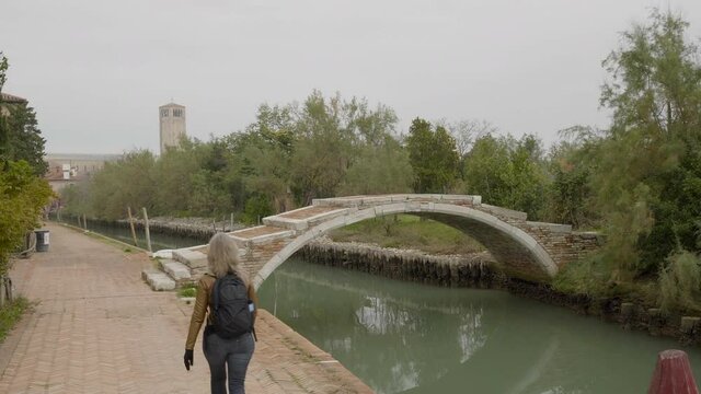 Woman crossing Ponte del Diavolo over Maggiore Canal in Torcello, Italy