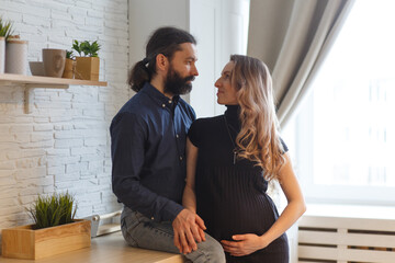 Man embracing pregnant partner in kitchen.