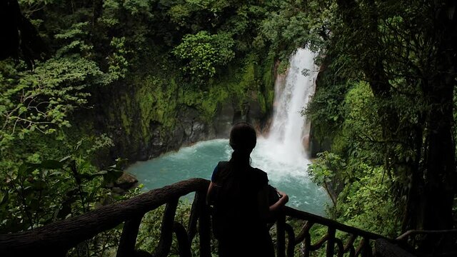 Girl looking at Catarata Rio Celeste in Parque Nacional Volc&aacute;n Tenorio, Costa Rica. Low angle, parallax movement, slow motion, HD.