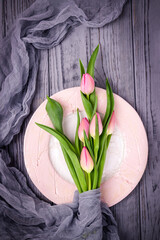 Pink tulips and a ceramic plate on a gray background, top view, free space