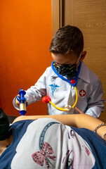 niño pequeño vestido de doctor con mascarilla  pasando consulta y poniendo vacuna de inyección en el brazo a una mujer