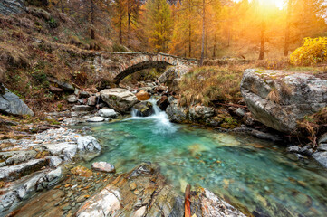 Fototapeta na wymiar Small waterfall and ancient bridge in autumn forest