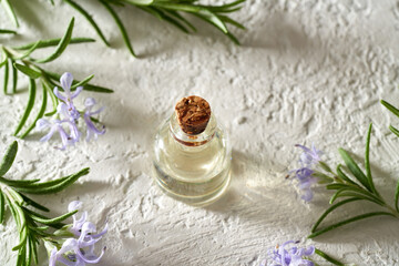 A bottle of essential oil with blooming rosemary twigs on white background