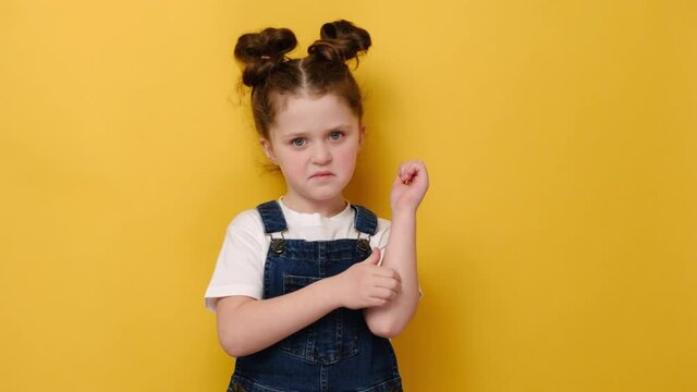 Portrait of unhappy little caucasian preschool girl scratching an itch with hand, isolated on yellow studio background. Kid suffers from allergy. Sensitive skin, food allergy symptoms, irritation