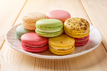 Set of multicolored macaroons on a white plate over wooden table. Colorful macaron cakes variety. Delicious french dessert. Sweets of almond flour with a delicate cream.
