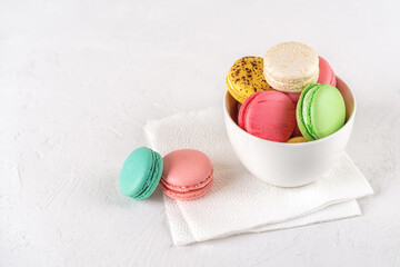 Multicolored macaroons in a white ceramic bowl on a light background. Colorful macaron cakes variety. Delicious french dessert. Sweets of almond flour with a delicate cream. High key image.