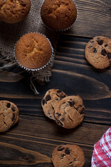 Morning breakfast vanilla muffins in white paper cups on a beautiful towel, close-up, with chocolate cookies. Wooden background.