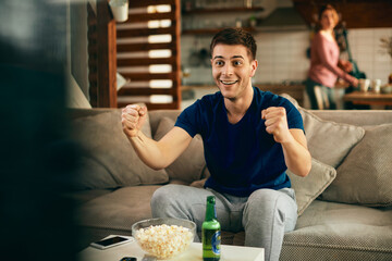 Young excited man watching sports match on TV at home.
