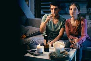Young couple drinking wine while watching TV at night at home.