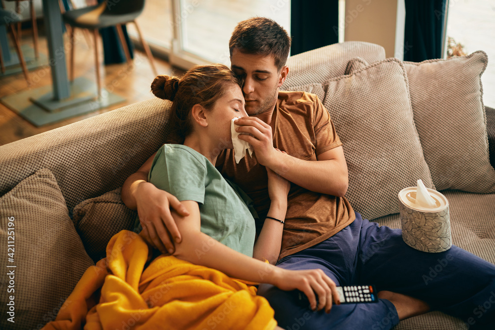 Wall mural Caring man wipes girlfriend's tears while watching sad movie on TV at home.