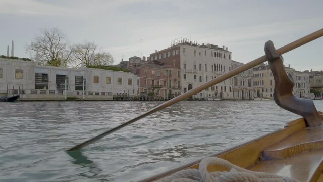 Close-up of gondolas oar moving in oarlock against Venetian townhouses.