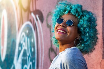portrait of young smiling black afro american woman with blue hair and sunglasses outdoors - Powered by Adobe