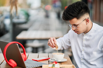 Fototapeta premium young man drinking a coffee in a coffee shop with a laptop and headphones on the table