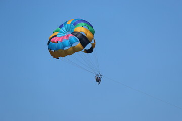 Gliding using a colorful parachute on the background of blue sky.