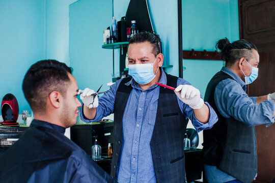 mexican man stylist with facemask cutting hair to a client in a barber shop in Mexico city in coronavirus pandemic