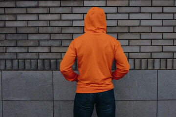Man in orange hoodie standing against brick wall background