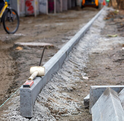 Concrete curbs are cemented along an evenly stretched line against the backdrop of a washed-out work area.