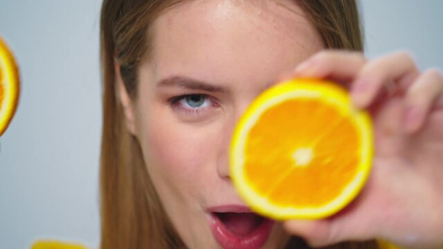 Closeup cheerful woman having fun with two orange slices at camera in studio. 