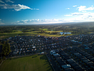 Fototapeta premium Aerial photograph of suburban sporting field and housing estate at sunset, with blue sky and white clouds.