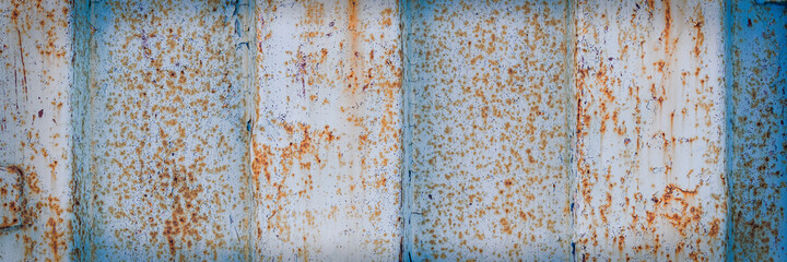 The texture of rusted metal painted in blue. Rough metal surface with rust. Rusty metal wall of a shipping container. Wide panoramic background for design.