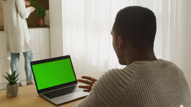 Young mixed-race couple in their apartment with an african american man sitting in front of a green screen laptop on a video call
