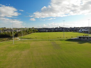 Aerial photograph of suburban sporting field and housing estate at sunset, with blue sky and white clouds.