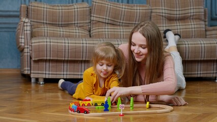 Mother with little daughter child girl riding toy train on wooden railway blocks board game at home