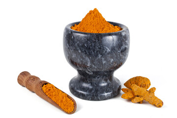 Turmeric powder spice heap in a black stone bowl with turmeric roots and bamboo scoop isolated on a...