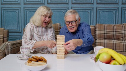 Retired senior couple spending time together playing game with wooden blocks on table in living room