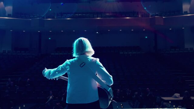 Young blonde girl white top finish song playing guitar on lonely empty stage sound checking small audience social distancing public clapping clap hands applause performance show stage lights excited