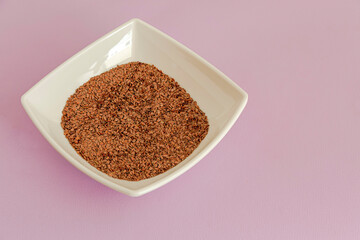 Flaxseeds in a white plate on a lilac table in the background.  