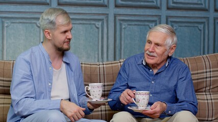 Different male generations family of senior father and adult son or grandson relaxing, drinking tea