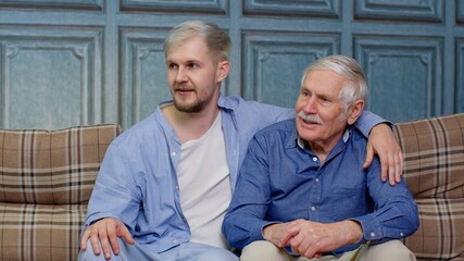 Family of senior father and adult son or grandson having conversation chatting relaxing on couch