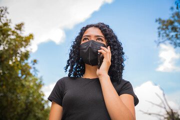 Fototapeta premium young woman with curly hair talking on the phone, she wears a black mask