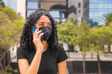 young woman with curly hair talking on the phone, she wears a black mask