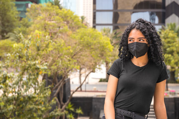 Young woman with curly hair is sitting. He is wearing a black mask