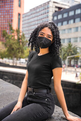 Young woman with curly hair is sitting. He is wearing a black mask