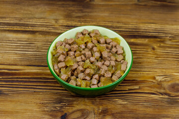 Canned food for cats or dogs in green ceramic bowl on wooden floor