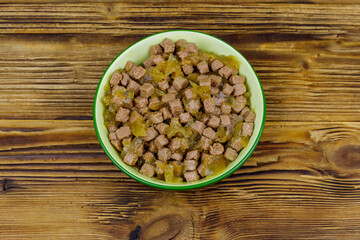 Canned food for cats or dogs in green ceramic bowl on wooden floor. Top view