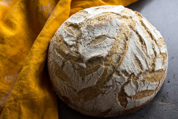 White round bread with leaves pattern on the top. Yellow linen fabric on background. Sourdough bread close up photo. 