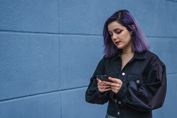 Fototapeta premium Young woman with purple hair using her cell phone and walking