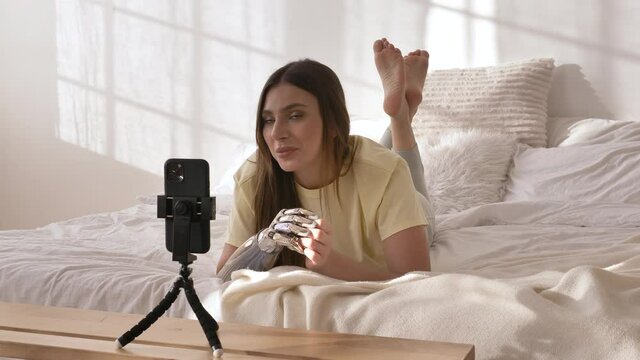 Positive woman with contemporary bionic arm shoots new video for blog with smartphone on bed in room at home closeup