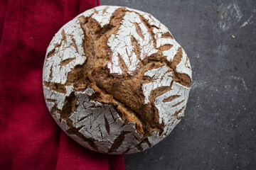 Tasty bread close up photo. Round sourdough bread with beautiful pattern on the top. Linen fabric towel on background. Homemade bread on a table. 
