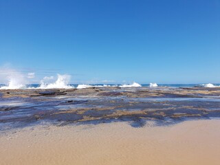 Waves crashing over rocks on sunny blue sky day, Austimere Beach, NSW, Australia