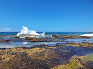 Waves crashing over rocks on sunny blue sky day, Austimere Beach, NSW, Australia