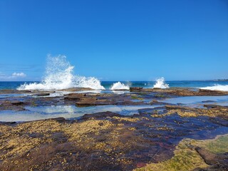 Waves crashing over rocks on sunny blue sky day, Austimere Beach, NSW, Australia