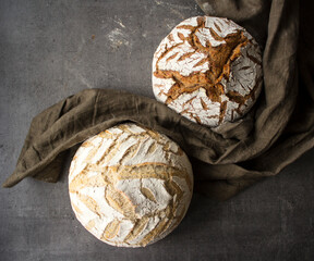Two breads on dark linen fabric. Grey textured background with copy space. Home bakery. Artisan bread scoring ideas. 