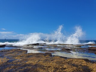 Waves crashing over rocks on sunny blue sky day, Austimere Beach, NSW, Australia
