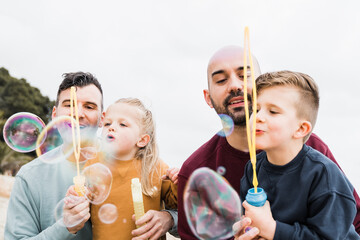 Gay parents and sons having fun with soap bubbles on the beach during summer vacation - Lgbt family...