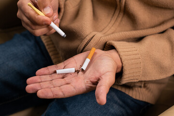 Detail shot of the hands of a man, holding a broken cigarette in one hand and a plastic stop-smoking cigarette in the other